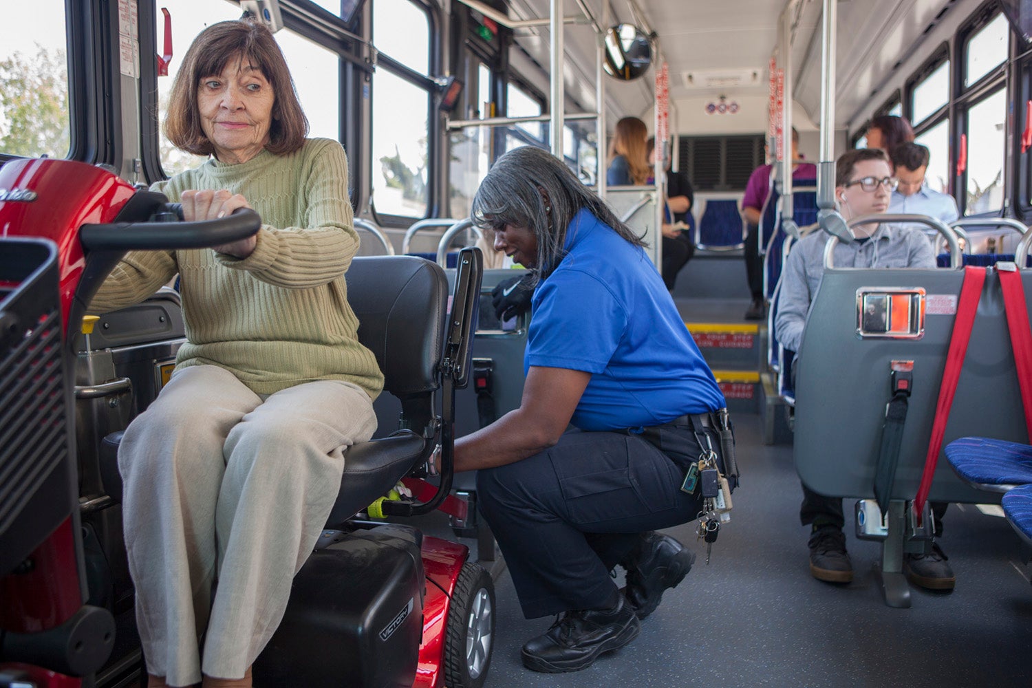 woman on mobility scooter getting buckled in by bus driver