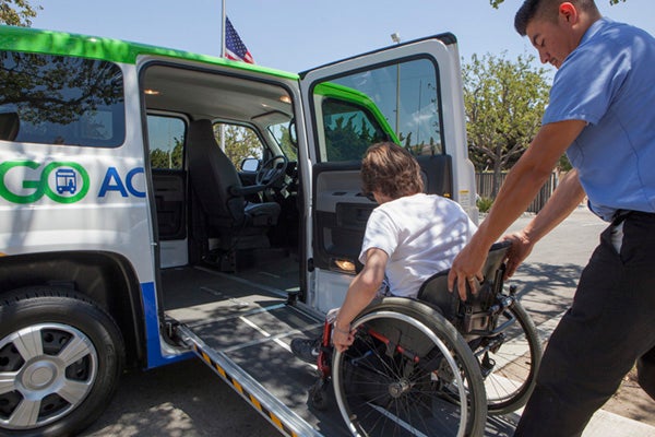 paratransit driver pushing person in wheelchair up ramp into van